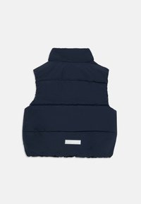 Tamsiai mėlynas pūkinis liemenė su aukštu apykakle, horizontaliai quilted dizainu ir atspindinčia detalė užpakalyje, pagaminta iš minkštos, patvarios medžiagos.