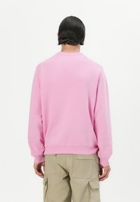 Sweatshirt rose avec un col rond et des poignets côtelés. Présente une texture lisse et une coupe décontractée. Porté avec un pantalon cargo beige.