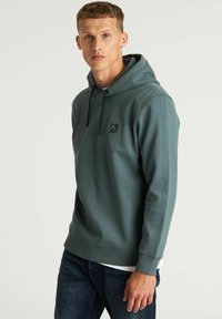 Hoodie in gedempt teal, gemaakt van zacht materiaal. Heeft een voorkantzak, een klein logo-label en ribbels aan de mouwen voor een stevige pasvorm.