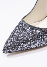 Escarpin noir pailleté à bout pointu, présentant une surface texturée de paillettes scintillantes et une doublure intérieure lisse et claire.