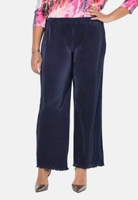 Navy corduroy levele-gait suunnikkaat, elastisella vyötäröllä ja aallotetulla helmalla, yhdistettynä hopeisiin korkokenkiin. Teksturoitu pinta on näkyvissä.