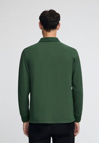 Dunkelgrünes Langarmhemd mit Kragen, aus glattem Stoff gefertigt; hat einen geraden Saum und anliegende Manschetten. Keine sichtbaren Muster oder Akzente.