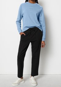 Sudadera azul claro con cuello redondo, mangas raglán largas y texto sutil. Pantalones negros ajustados con pinzas frontales y cintura elástica. Zapatillas marrón claro.