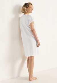 Hvid, knælang kjole med korte, optrullede ærmer. Lavet af blødt stof, med en enkel, lige snit og minimal dekoration.