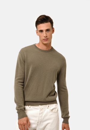 Maglione lavorato a maglia in verde oliva, colletto a giro, maniche lunghe, texture morbida, polsini e orlo a costine, abbinato a pantaloni corti bianchi.