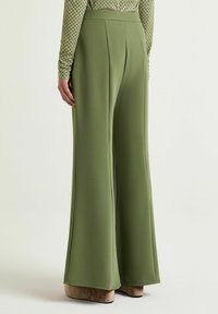 Pantaloni a gamba larga in tessuto verde liscio, con vita alta, pieghe e silhouette fluida. Accostati a scarpe beige con plateau.