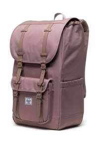 Un sac à dos Herschel rose poussière avec poche avant, bretelles à double boucle, dos rembourré et poignée de transport supérieure, présenté sous un léger angle latéral.