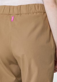 Beżowe spodnie elastyczne z gładkiego, lekkiego materiału. Oferują różową metkę marki w pasie oraz prosty, elegancki design.