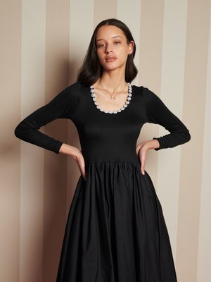 Vestido negro con mangas largas, corsé ajustado y falda voluminoso. Presenta un escote redondeado adornado con acentos florales.
