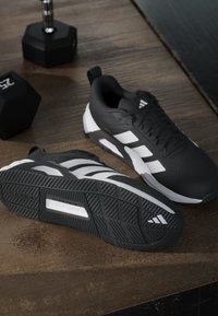 Black athletic shoes with white stripes, textured mesh upper, padded collar, and a rubber outsole featuring a herringbone pattern for traction.