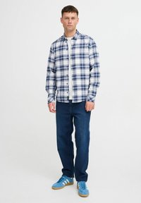Camicia a quadri blu, bianca e navy; con bottoni sul davanti e maniche lunghe. Abbinata a jeans scuri in denim e sneakers blu.