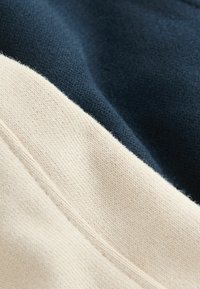 Suéter con un diseño de bloques de color azul marino y crema; suave tejido de algodón con un acabado texturizado y costuras visibles en las uniones.