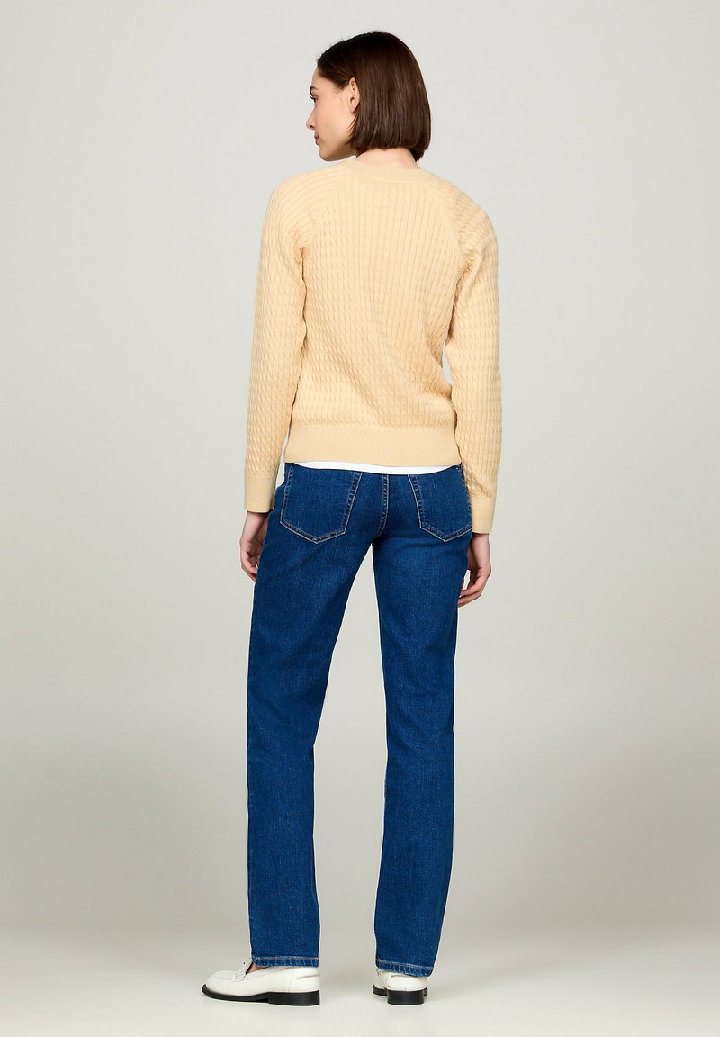 Beżowy sweter o fakturze z detalami w prążki, w połączeniu z niebieskimi dżinsami i białymi butami. Sweter ma okrągły dekolt i dopasowane mankiety.