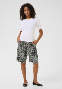 Top ajustado blanco de manga corta combinado con pantalones cortos de estampado de leopardo verde y negro. Los pantalones cortos tienen un corte holgado y bolsillos laterales. Se llevan unos zapatos de ballet negros.