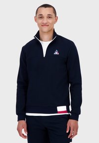 Felpa blu navy con zip a un quarto, dotata di un piccolo logo sul petto e una striscia multicolore sull'orlo. Materiale morbido in misto cotone.