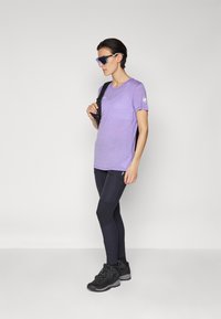 T-shirt atletica viola a maniche corte, abbinata a leggings neri con texture varie e scarponi da trekking neri con lacci.