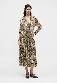 Φόρεμα με λεοπάρ σχέδιο, μακρυμάνικο, με V-λαιμόκοψη και δεμένη μέση από απαλή υφή. Φούστα που φαρδαίνει με ροή υφάσματος. Μαύρα επίπεδα παπούτσια.