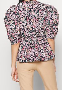 Top peplum floral con mangas abullonadas, con un fondo azul marino oscuro y flores vibrantes en rosa, blanco y verde. Tela de algodón texturizada.