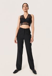 Bralette de encaje negro con un borde festoneado combinado con pantalones negros de tiro alto. Tejido suave, ajuste entallado y sin herrajes visibles.