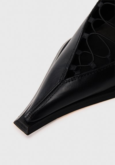Μαύρο δερμάτινο παπούτσι με μυτερή μύτη, περίτεχνα πλεγμένες λεπτομέρειες στο επάνω μέρος και κομψή, χαμηλού προφίλ σόλα.