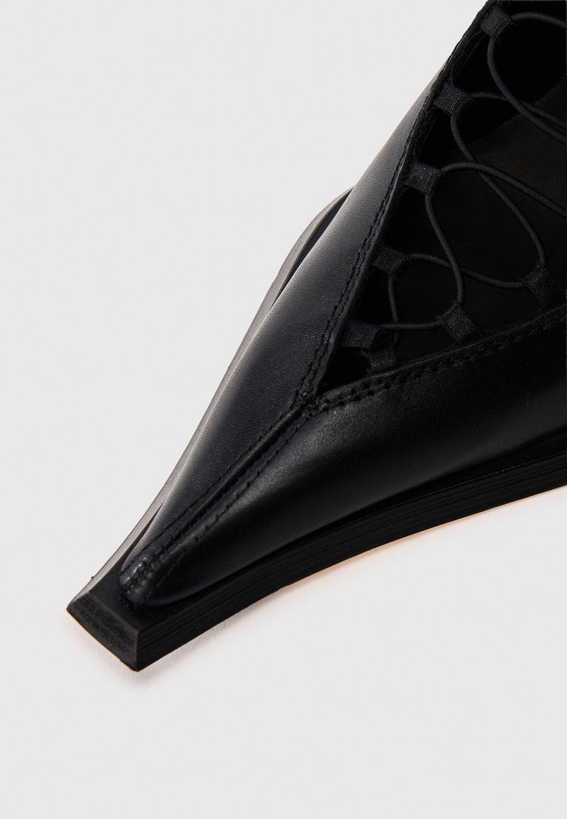 Schwarzer Lederschuh mit spitz zulaufender Schuhspitze, aufwändigem geflochtenem Muster am Obermaterial und einer eleganten, flachen Sohle.