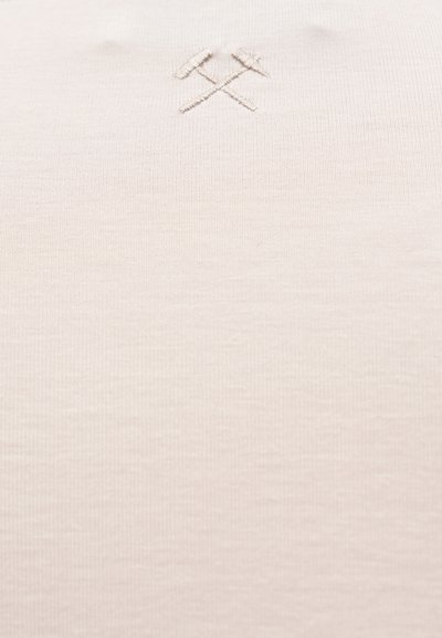 Μπεζ ύφασμα με διακριτικό κεντημένο σύμβολο σταυρωμένου σφυριού και αξίνας κοντά στο πάνω κέντρο.