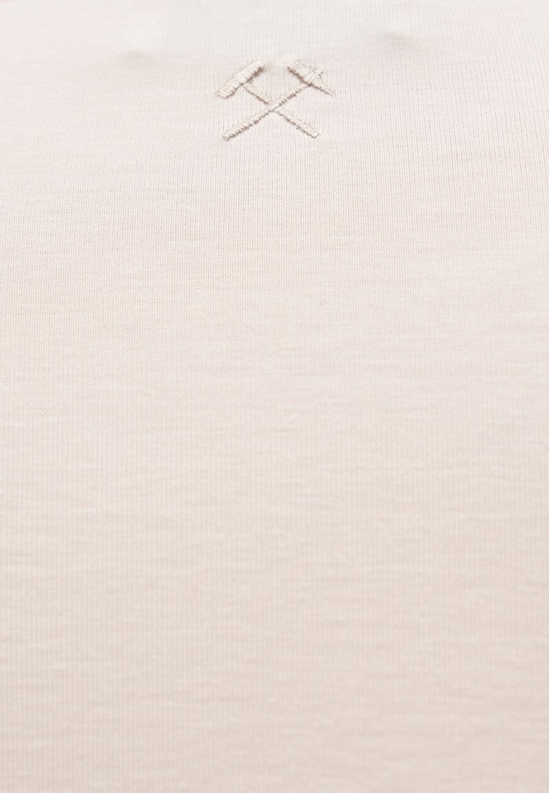 Tissu beige avec un symbole délicatement brodé de marteau et pioche croisés près du centre en haut.