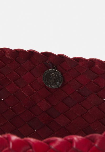 Szőtt piros bőrtáska, hullámos szélekkel. Jellemzője egy fém charm, amelyen az áll: "Szent Kristóf, Védelmezz Minket." Barázdált felület.