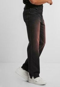 Vaqueros de mezclilla negra con un diseño de pierna recta, que cuentan con cinco bolsillos, un desvanecimiento sutil y herrajes de metal. Combinados con zapatillas blancas.