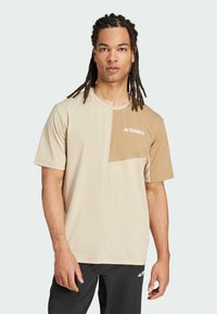 Beige short-sleeve t-shirt with a darker beige chest panel. Features a "TERREX" logo in white at the left side. Smooth texture and relaxed fit.