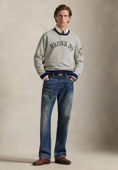 Gray sweatshirt with "BRONX NY" text, navy ribbed collar and cuffs. Worn with light blue jeans and brown leather shoes, featuring a textured finish.