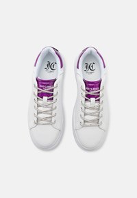 Witte sneakers met paarse metalen accenten en zilveren veters, voorzien van een gladde textuur en een ronde neus.