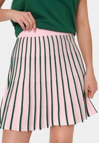 Jupe plissée tricotée en rose avec des rayures verticales vertes, une taille ajustée et un ourlet évasé. Texture douce avec un design classique.