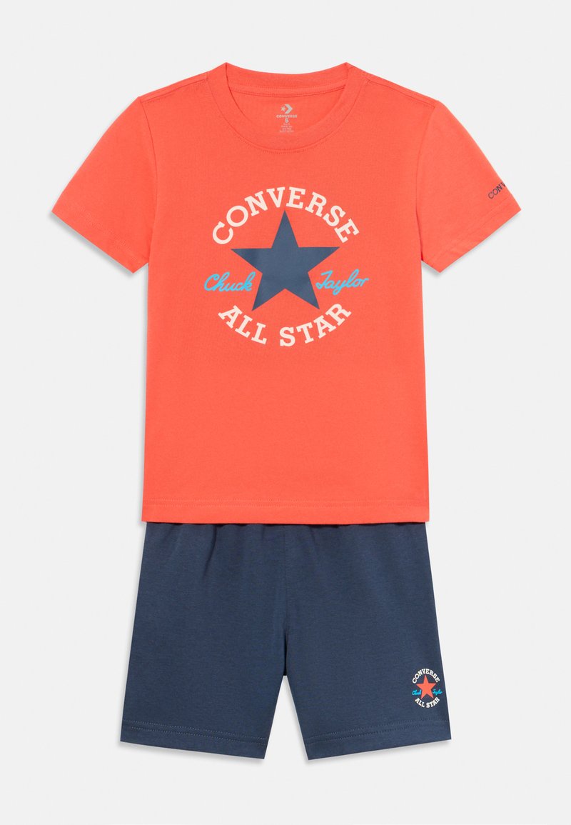 T-shirt di cotone corallo con grafica a stella blu e testo bianco, abbinata a pantaloni corti blu navy con logo sulla gamba.