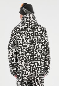 Mustat ja valkoiset kuviot, joissa on huppu, rohkealla tekstillä eri kokoisina. Sileä rakenne; yhdistettynä yhteensopivaan beanie-hattuun ja suojalaseihin.