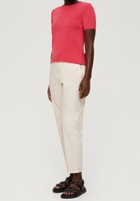 Kortärmad rosa stickad t-shirt, ihop med krämfärgade tapered byxor och svarta sandaler med remmar. Slät textur, avslappnad passform och enkel design.