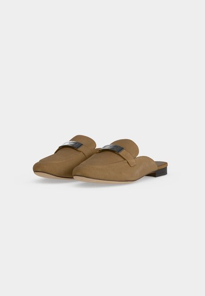 Paire de mocassins beiges à enfiler avec petits talons et ornements métalliques argentés sur le dessus, présentée sur un fond clair uni.