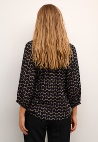 Navybluse mit beigem abstraktem Muster, Dreiviertelärmel, lockere Passform, weicher Stoff und geraffte Bündchen. Tragen mit schwarzen Hosen.