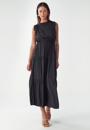 Black maxi dress with tiered design, soft fabric, sleeveless with shoulder ties, cinched waist, and flowing skirt. Worn with light strappy heels.