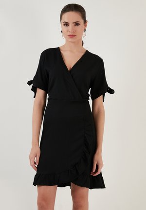 Black wrap dress with short sleeves, ruffled hem, textured fabric, and ties at the sleeves. Fitted design with a v-neckline.