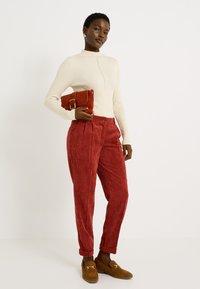 Haut à manches longues écru à côtes, pantalon taille haute en velours côtelé rouge, mocassins couleur beige et petite pochette rouge avec un détail de boucle en métal.