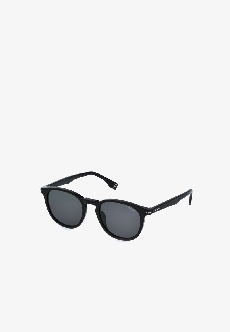 Lunettes de soleil rondes noires avec verres foncés et branches fines comportant un petit logo sur les branches, sur fond blanc.