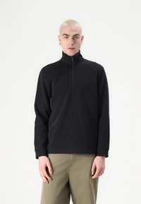 Schwarzer Reißverschluss-Pullover aus einem weichen, strukturierten Stoff mit langen Ärmeln. Verfügt über einen hohen Kragen und ein schlankes Design.