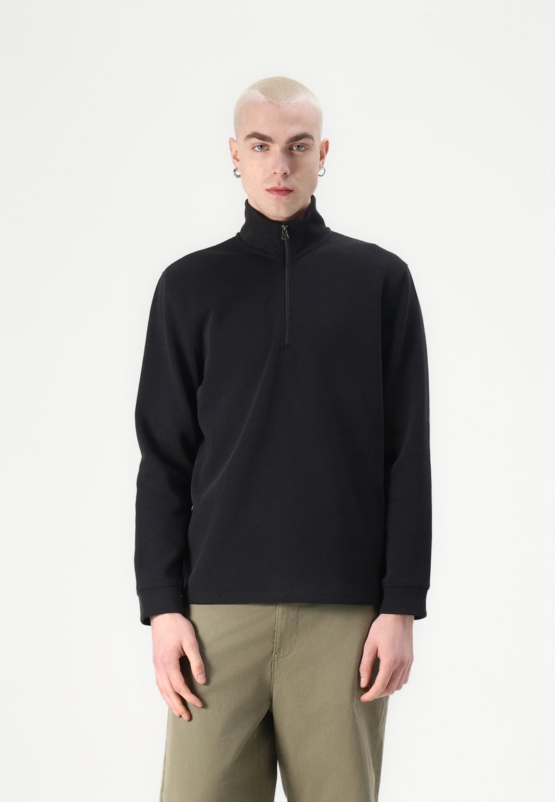 Schwarzer Reißverschluss-Pullover aus einem weichen, strukturierten Stoff mit langen Ärmeln. Verfügt über einen hohen Kragen und ein schlankes Design.
