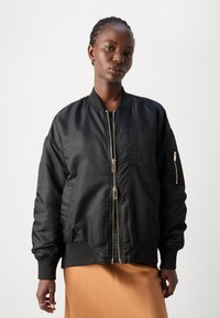Schwarze Bomberjacke mit glatter, glänzender Textur, Reißverschluss vorne und gerippten Bündchen. Sie verfügt über Seitentaschen und eine aufgesetzte Tasche auf der Brust.