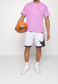 Basketbalový outfit se skládá z růžového bavlněného trička s logem "Just Do It", bílých šortek s černými akcenty a bílých sportovních bot.