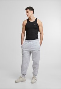 Zwarte mouwloze tanktop en grijze joggingbroek met een elastische tailleband, voorzien van een bedrukte logo. Draagt het met lichtgekleurde sneakers.