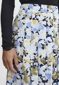 Blommönstrad kjol i ljusblått, med veck, knappar och färger som marinblått, gult och grönt på ett strukturerat tyg.