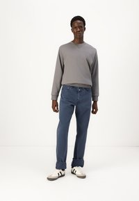 Grau Sweatshirt mit Rundhalsausschnitt, blaue gerade Jeans und weiße Sneaker mit schwarzen Streifen. Einfaches Design, lässige Passform.