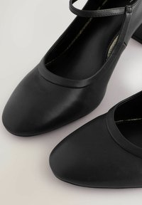 Pantofi negri cu toc înalt, exterior din piele netedă, vârf rotund și baretă subțire la gleznă. Designul are o siluetă simplă, clasică.